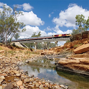 Long train crossing a bridge over a dry creek bed.