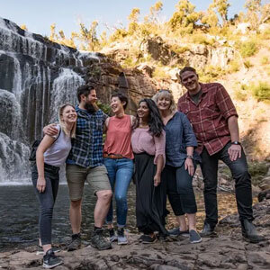 Group of friends smiling in front of waterfall.