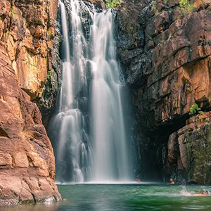 A stunning waterfall cascading into a pool surrounded by rocky cliffs, with people swimming below.