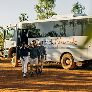 Travelers near "Outback Spirit" bus under trees.