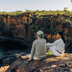 A couple relaxing on a rock, enjoying breathtaking views of a cascading waterfall in the distance.