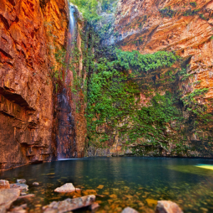 A waterfall cascading down a red rock cliff into a clear gorge.