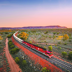 The Ghan travelling through the MacDonnell Ranges under pink skies